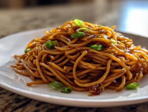 A close-up of a generous serving of glossy, brown garlic noodles topped with fresh green scallions.