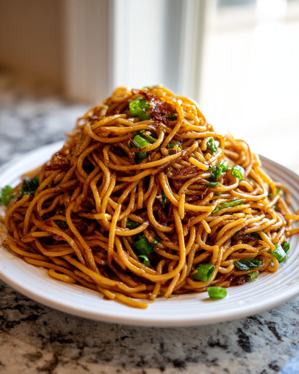 A tall mound of glossy, brown garlic noodles topped with chopped green onions on a white plate.