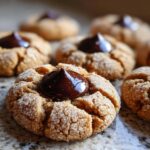 A close-up of a soft, sugar-coated peanut butter kiss cookie topped with melted chocolate.