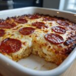 Close-up of a baked pepperoni pizza dip in a white dish with a serving removed, showing melted cheese.