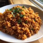 Close-up of a white bowl filled with rich, orange-red Spanish rice, garnished with fresh cilantro.