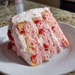 Close-up of a moist slice of pink strawberry cake layered with white frosting and visible strawberry pieces.