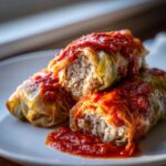 Close-up of two Amazing Stuffed Cabbage Rolls cut open to show rice and meat filling, topped with rich tomato sauce.