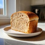 A freshly baked loaf of whole wheat bread, cut to show the soft, airy crumb, resting on a plate.
