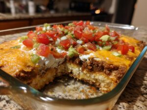 A baked 7 layer dip in a glass dish with a section removed, showing layers of ingredients topped with fresh tomatoes and avocado.