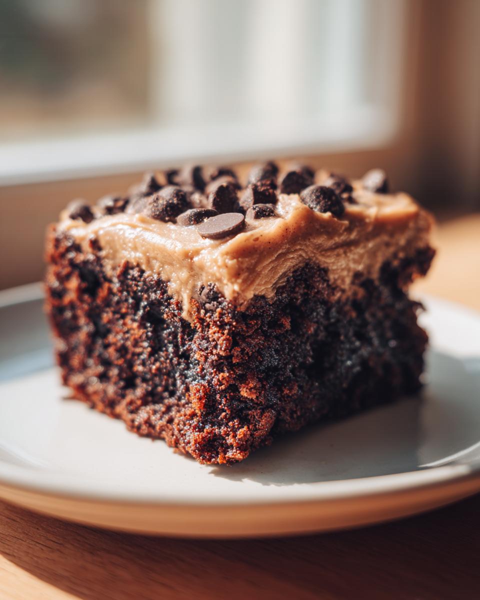 A close-up of a dense, dark chocolate banana bread brownies slice topped with peanut butter frosting and chocolate chips.