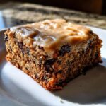 A close-up of a moist square of banana bread brownies studded with chocolate chips and topped with creamy brown frosting.