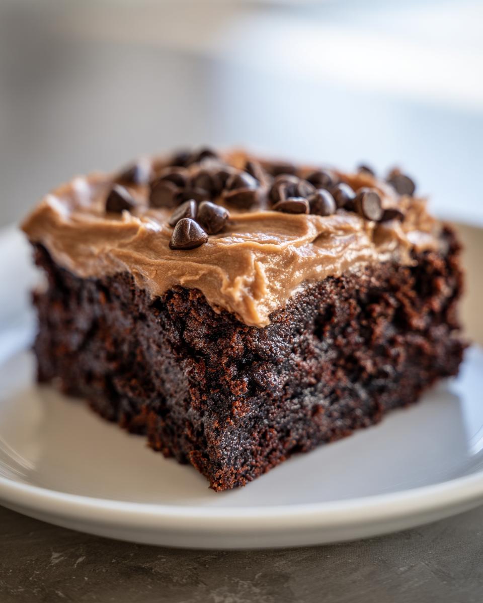 Close-up of a moist, dark chocolate banana bread brownies slice topped with peanut butter frosting and chocolate chips.