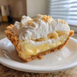 A close-up of a perfect slice of banana cream pie showing the crust, creamy filling, banana slices, and whipped topping.