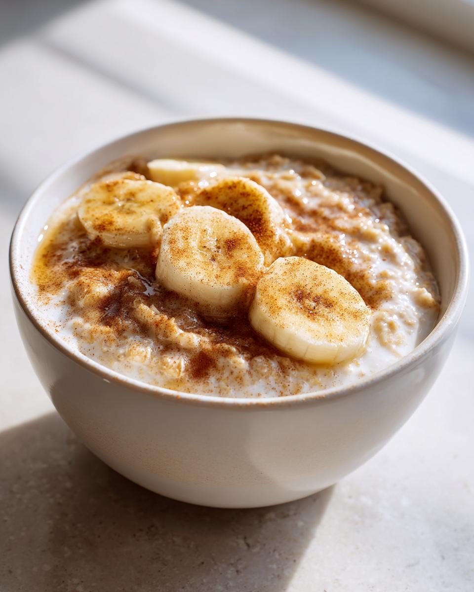 Close-up of a creamy bowl of banana oatmeal topped with sliced bananas and cinnamon.