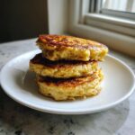 A stack of three golden-brown banana oatmeal pancakes served on a small white plate.