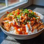 A close-up of a delicious buffalo chicken bowl layered over white rice, drizzled with ranch and topped with green onions.