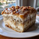 A close-up of a moist slice of butter pecan praline poke cake with creamy filling and pecan topping.