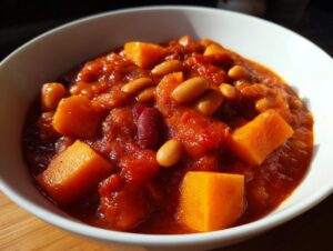 Close-up of vibrant, thick butternut squash chili featuring orange squash chunks, white beans, and kidney beans in a rich tomato base.