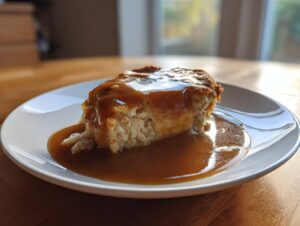 A slice of light-colored cake generously covered in thick, glossy brown gravy, served on a white plate.