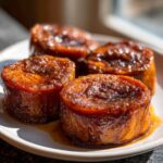 Close-up of four thick, round candied sweet potatoes glistening with a rich, dark brown glaze.