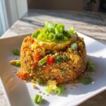 A molded serving of golden brown cauliflower fried rice topped with a fried egg and fresh green onions.