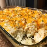 A close-up of a baked chicken and rice casserole topped with melted cheddar cheese and parsley in a glass dish.