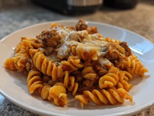 Close-up of cheesy chicken pasta featuring fusilli noodles coated in tomato sauce and topped with melted cheese.