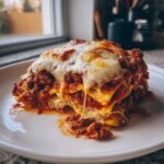A generous slice of ravioli lasagna covered in melted cheese and rich meat sauce, served on a white plate.