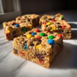 Close-up of a thick, chewy Christmas cookie bars square topped with colorful M&Ms and chocolate chips.