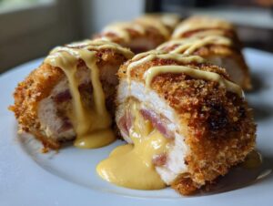 Close-up of sliced chicken cordon bleu showing crispy breading, ham, and oozing melted cheese sauce.