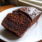 Close-up of two thick slices of rich, dark chocolate banana bread on a white plate.