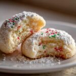 Two halves of a Christmas gooey butter cookie, dusted heavily with powdered sugar and topped with red and green sprinkles.