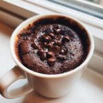 A rich, dark chocolate Cottage Cheese Microwave Brownie topped with melted chocolate chips in a white mug.