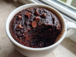 A rich, dark chocolate Cottage Cheese Microwave Brownie topped with melted chocolate chips in a white mug.
