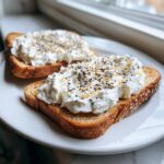 Two slices of toasted bread topped generously with creamy cottage cheese toast and everything bagel seasoning.