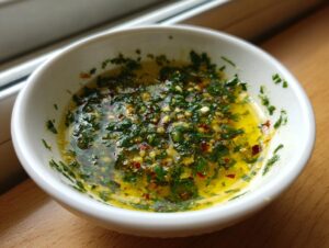 A white bowl filled with vibrant cowboy butter dipping sauce, featuring melted butter, fresh parsley, garlic, and red pepper flakes.