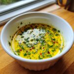 Close-up of bright yellow cowboy butter dipping sauce topped with fresh green herbs and red pepper flakes.