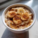 A white bowl filled with creamy banana oatmeal, topped with sliced bananas and a dusting of cinnamon.