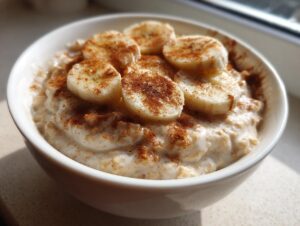 Close-up of a white bowl filled with creamy banana oatmeal, topped with sliced bananas and a dusting of cinnamon.