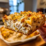 A thick slice of creamy chicken and wild rice casserole held up, showing shredded chicken, wild rice, and a cheesy, browned topping.