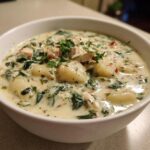 A close-up of a hearty bowl of creamy chicken and gnocchi soup, garnished with fresh parsley.
