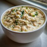 Close-up of a hearty bowl of creamy crockpot white chicken chili, featuring shredded chicken, white beans, and green herbs.