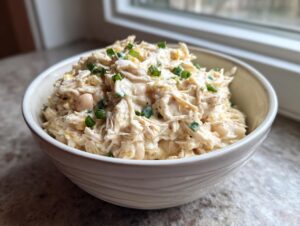 A bowl filled with creamy crockpot white chicken chili, featuring shredded chicken and white beans, topped with green onions.