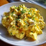 A close-up of creamy, bright yellow egg salad recipe topped generously with freshly chopped green chives.