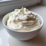 A close-up of fluffy, white cream cheese fruit dip swirled high in a small white bowl.