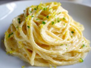 A beautiful mound of creamy lemon pasta, coated in a rich sauce and topped with bright yellow lemon zest and chopped parsley.