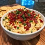 A creamy, cheesy neiman marcus dip served in a white bowl, generously topped with crispy bacon bits and chopped green onions.