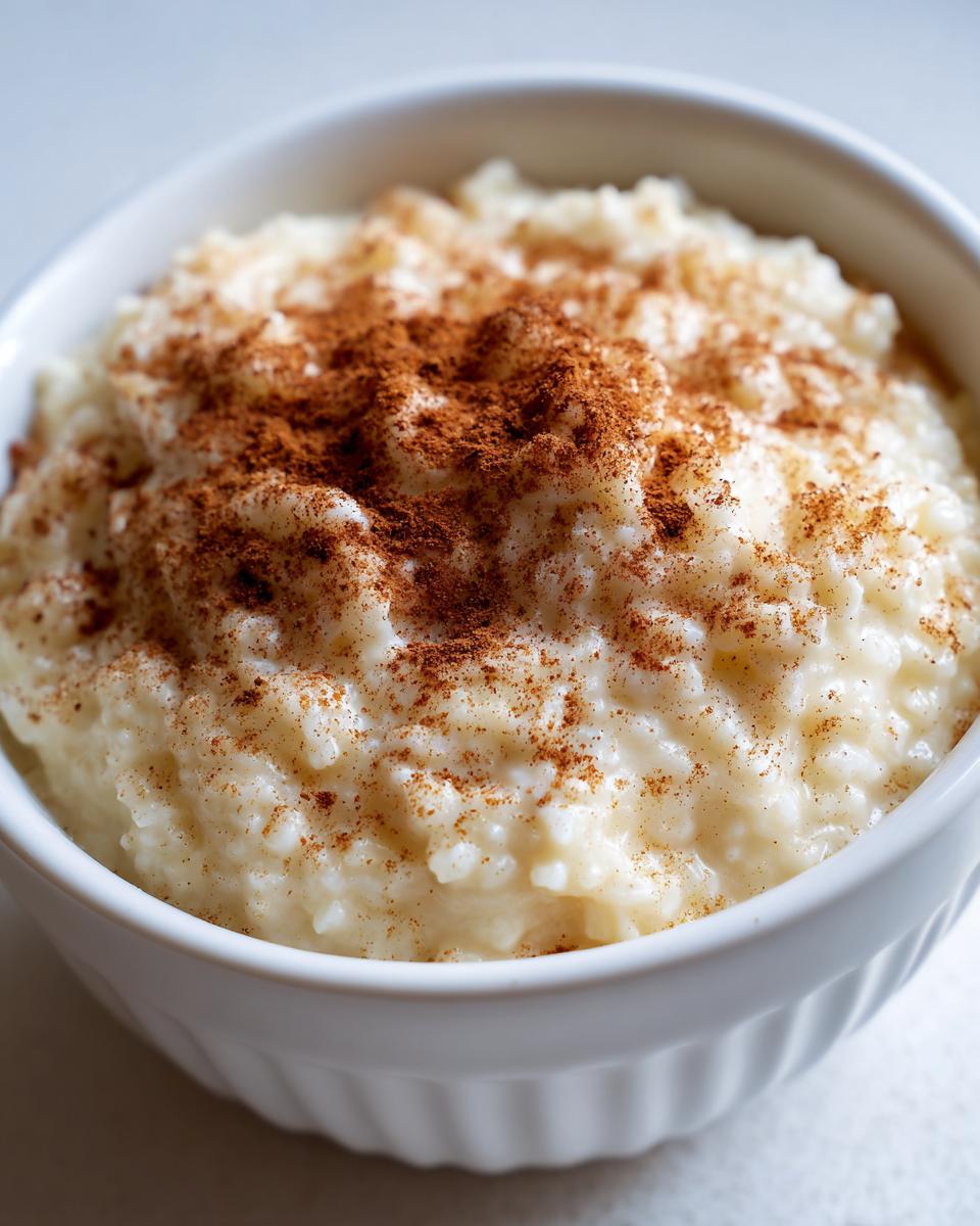 Close-up of creamy rice pudding served in a white bowl, generously dusted with ground cinnamon.