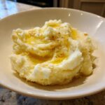 A serving of creamy roasted garlic mashed potatoes topped with melted butter and visible roasted garlic pieces.