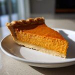 A close-up of a perfectly baked slice of sweet potato pie showing its creamy orange filling and flaky crust.