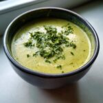 Close-up of a bowl of creamy, light green zucchini soup topped with chopped fresh parsley.