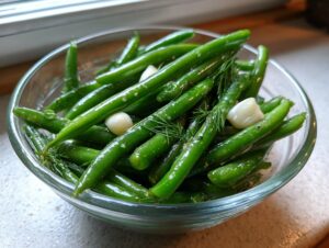 Close-up of bright green, crisp dilly beans in a glass bowl with whole garlic cloves and fresh dill fronds.