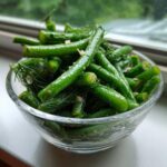 Close-up of bright green, crisp dilly beans seasoned with fresh dill and garlic in a clear glass bowl.