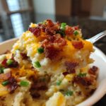 Close-up of a spoonful of creamy easy crockpot potato soup topped with melted cheddar cheese, bacon bits, and chives.